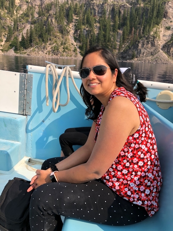 Girl with a red floral top sitting on a blue seat on a boat in Crater Lake