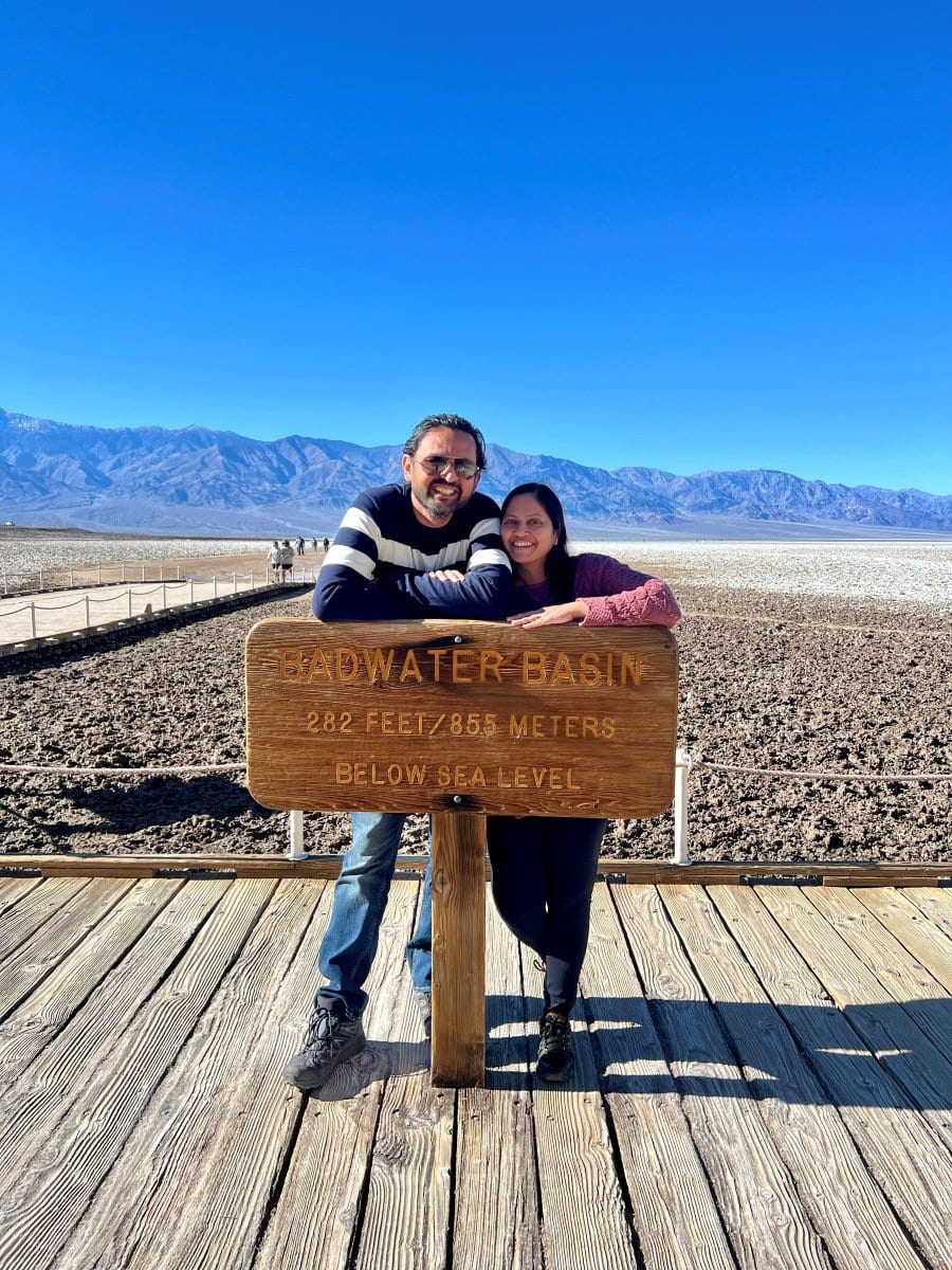 Couple posing at a sign that says Badwater Basin in death Valley National Park. Badwater Basin is a must visit in a one day in Death Valley itinerary. 