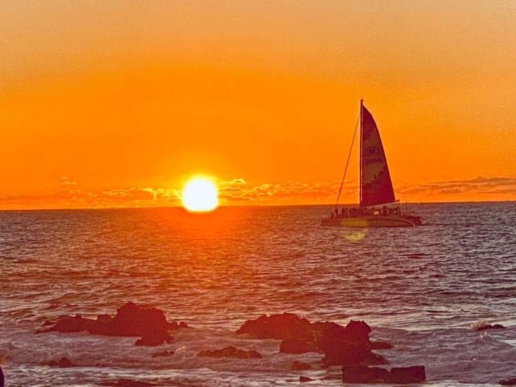 Catamaran sail boat in Hawaii ocean waters with sunset in the horizon.