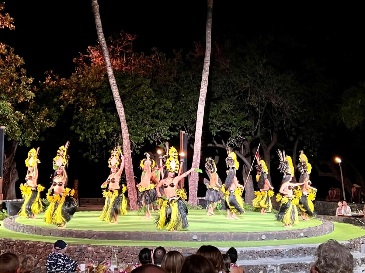 Group of female dancers wearing yellow and black Hawaiian hula dance costumes are doing hula dancing in a circle on a circular open air stage