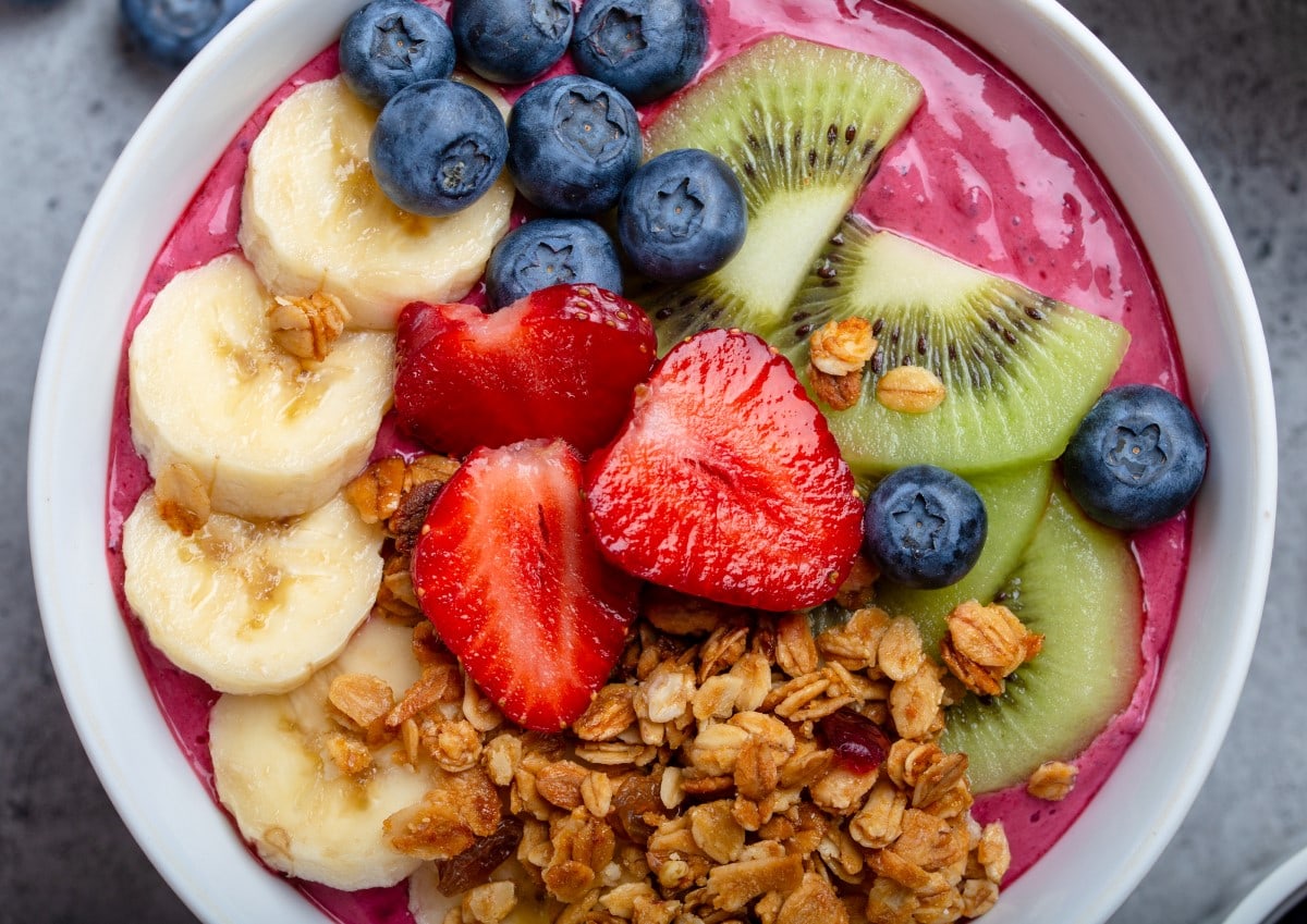Acai smoothie bowl topped with fresh fruits like bananas, strawberries, kiwi and granola