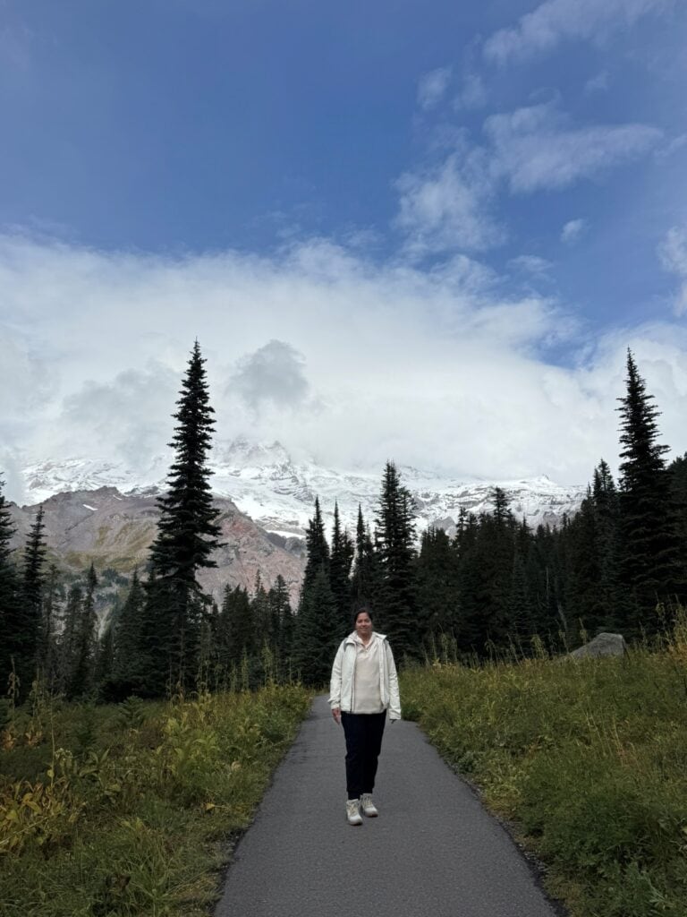 A girl posing on a hiking trail in Mt. Rainier with the mountain partly peeking in the backdrop