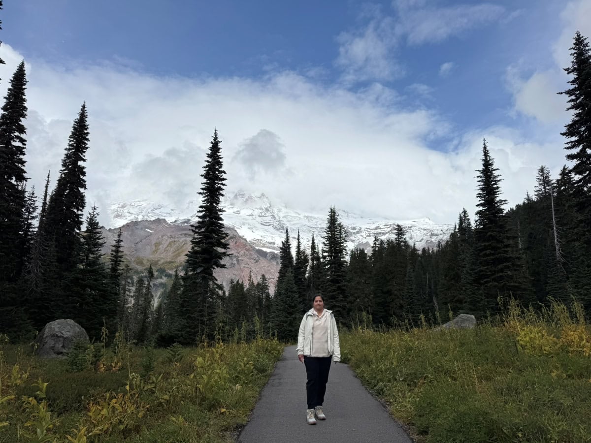 A girl posing on a hiking trail in Mt. Rainier with the mountain partly peeking in the backdrop