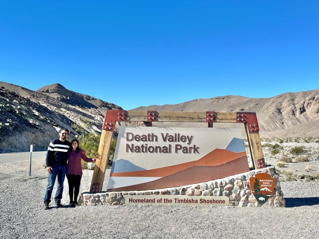 Couple posing next to Death Valley National Park Sign surrounded by desert landscape