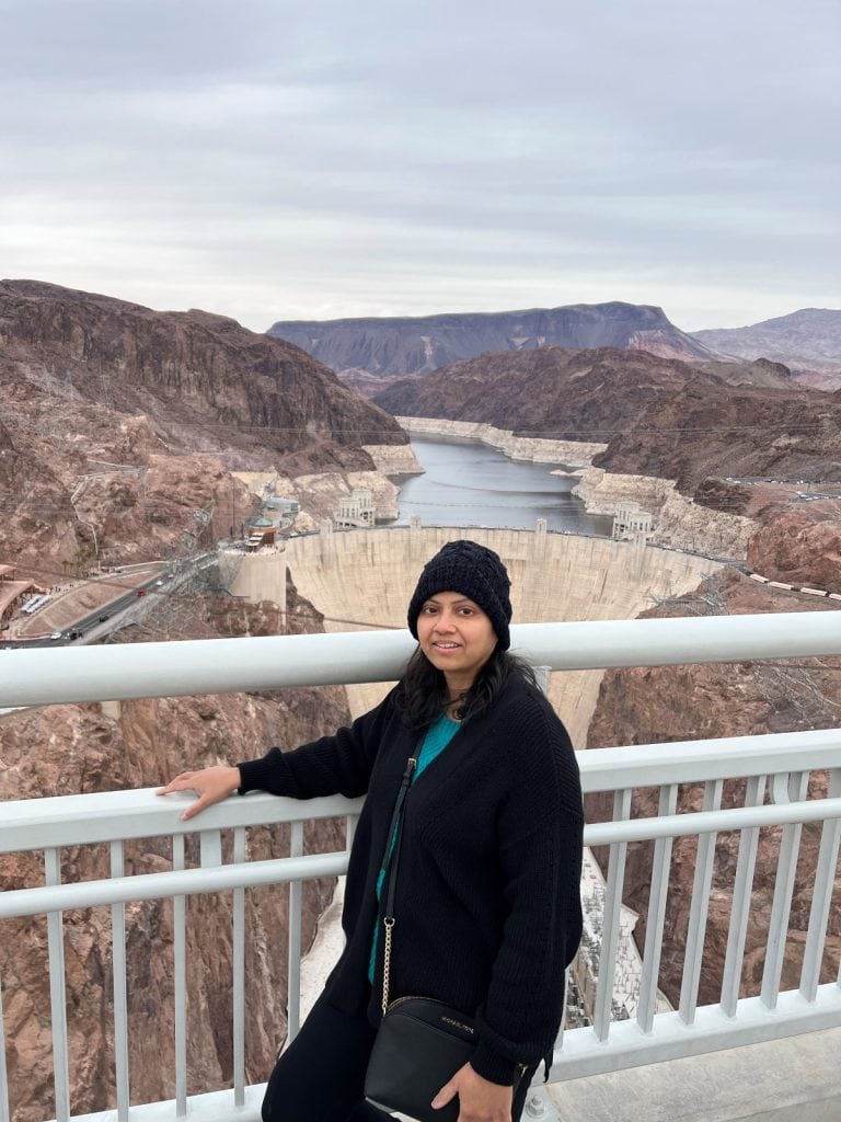 Girl in black outfit standing against the Memorial Bridge railing with Hoover Dam and Lake Mead in the background