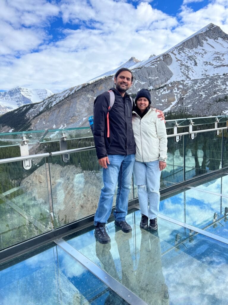 A couple posing on a a glass skywalk with mountain views in the backdrop