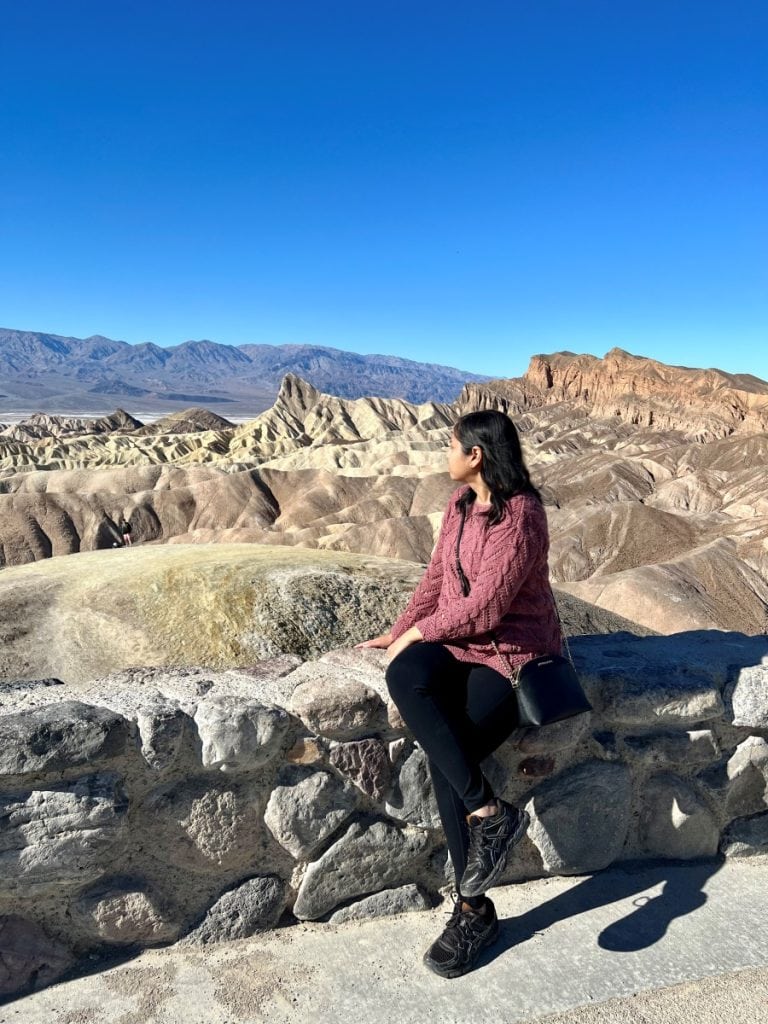 Girl sitting on a rock wall looking out at the badlands at Zabriskie Point in Death Valley National Park