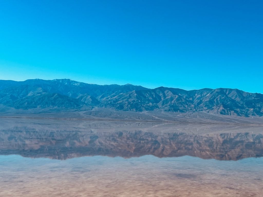 Shallow lake at Badwater Basin reflecting the surrounding mountain scenery in its still water