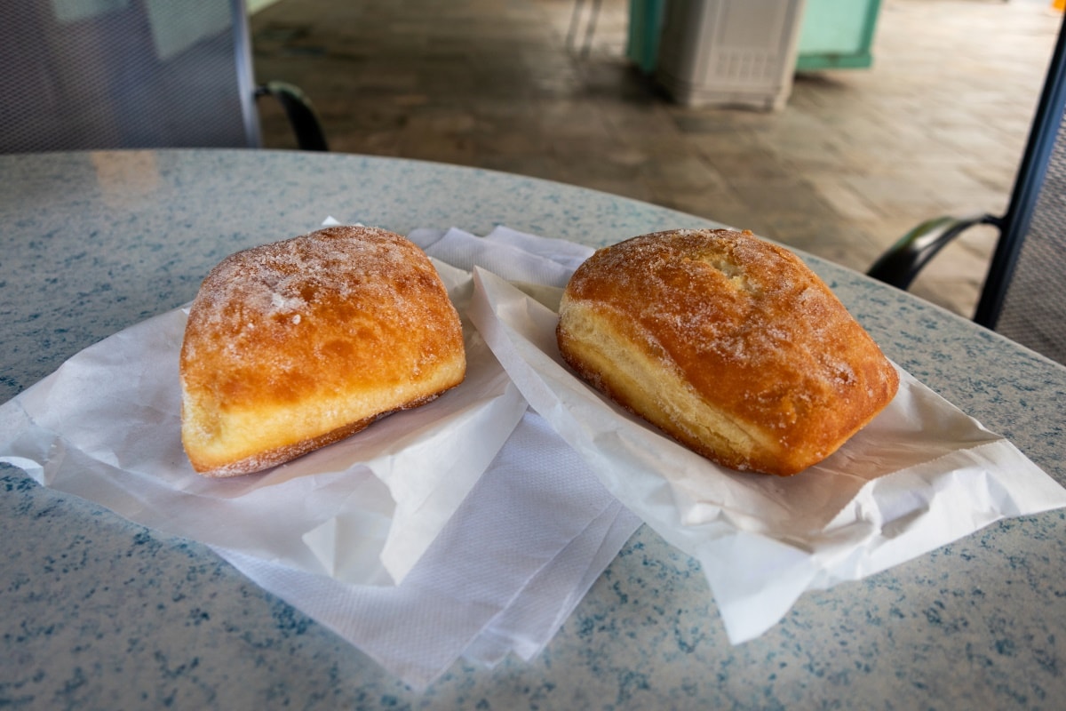 two malasadas (fried Portuguese donuts) placed on top of to-go bags